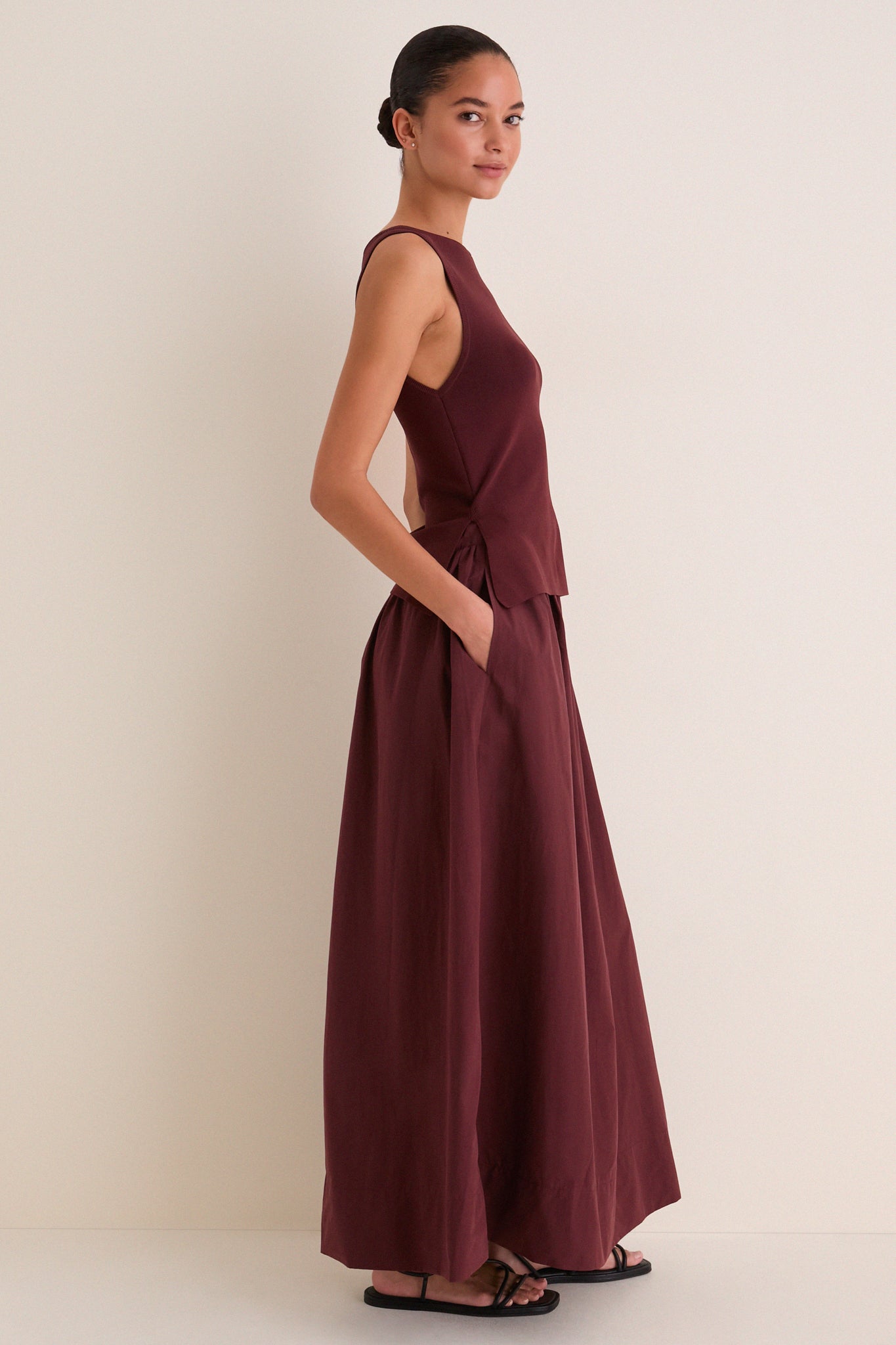 Model in profile wearing the Dark Cherry Boatneck Mix Media Midi Dress with sleek silhouette and side pockets, paired with black sandals for an effortless, high-end look.