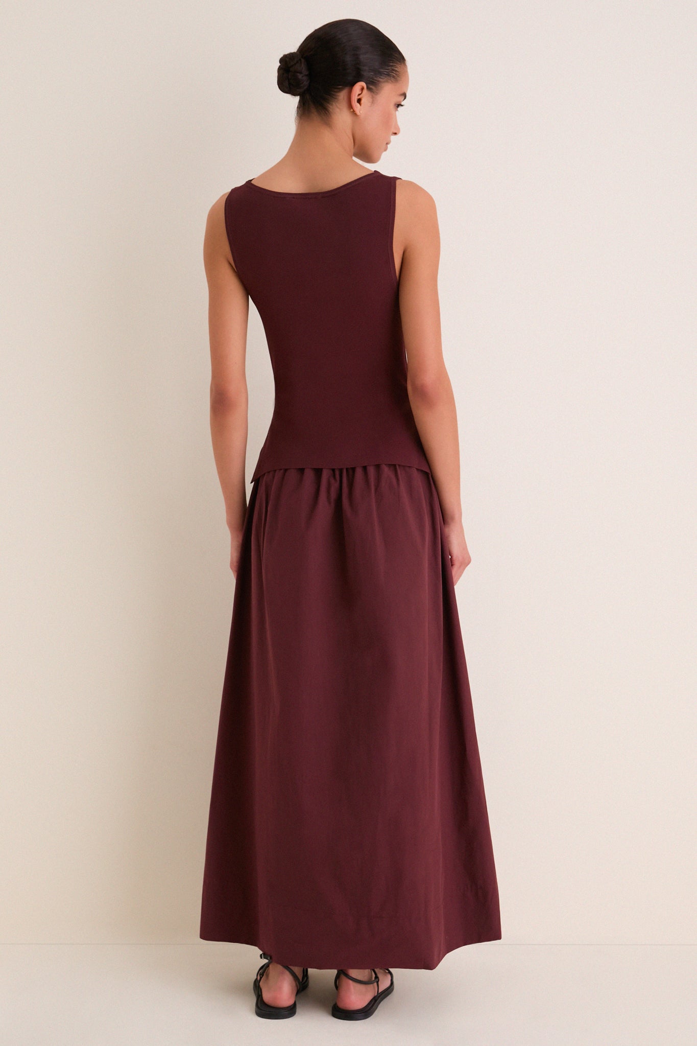 Back view of a model in a classic Dark Cherry Boatneck Mix Media Midi Dress, showcasing its effortless silhouette and gathered maxi-length skirt, styled with fun, high-end flair.