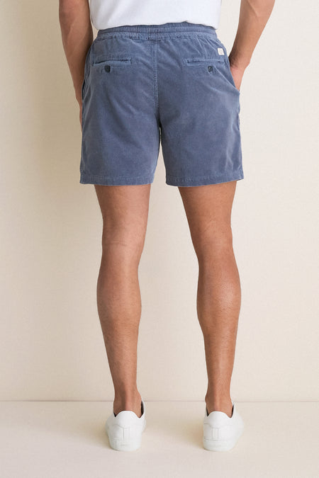 Back view of a person wearing classic, effortless Faded Navy Saturday Corduroy Shorts with button-flap pockets, paired with white sneakers. High-end, fun, and comfortable summer style.