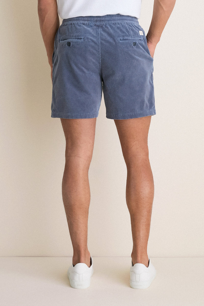 Back view of a person wearing classic, effortless Faded Navy Saturday Corduroy Shorts with button-flap pockets, paired with white sneakers. High-end, fun, and comfortable summer style.