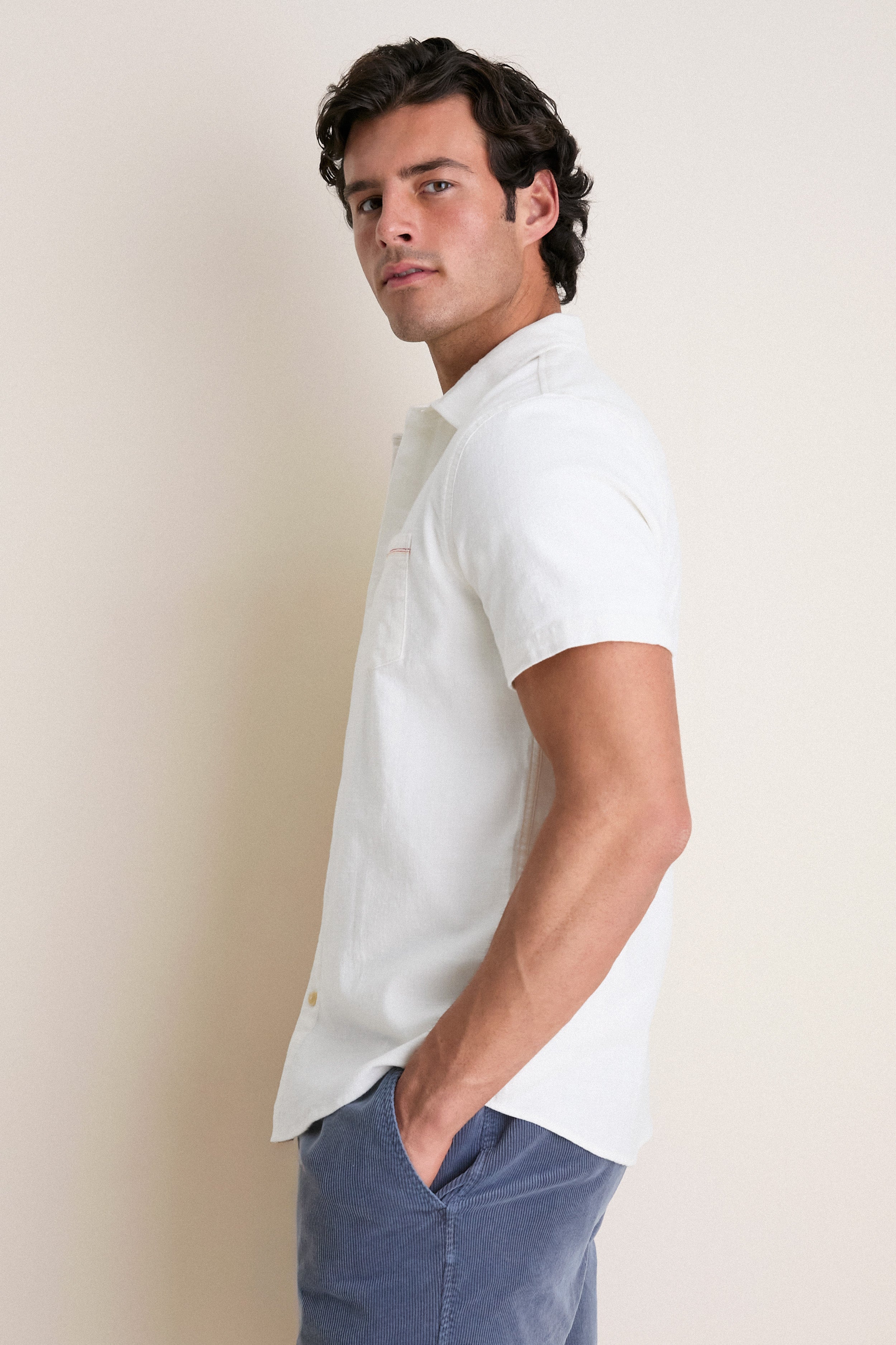 Young man in profile wearing the White Classic Stretch Selvage Shirt by Marine Layer, showcasing a classic, effortless style with short sleeves and a chest pocket.