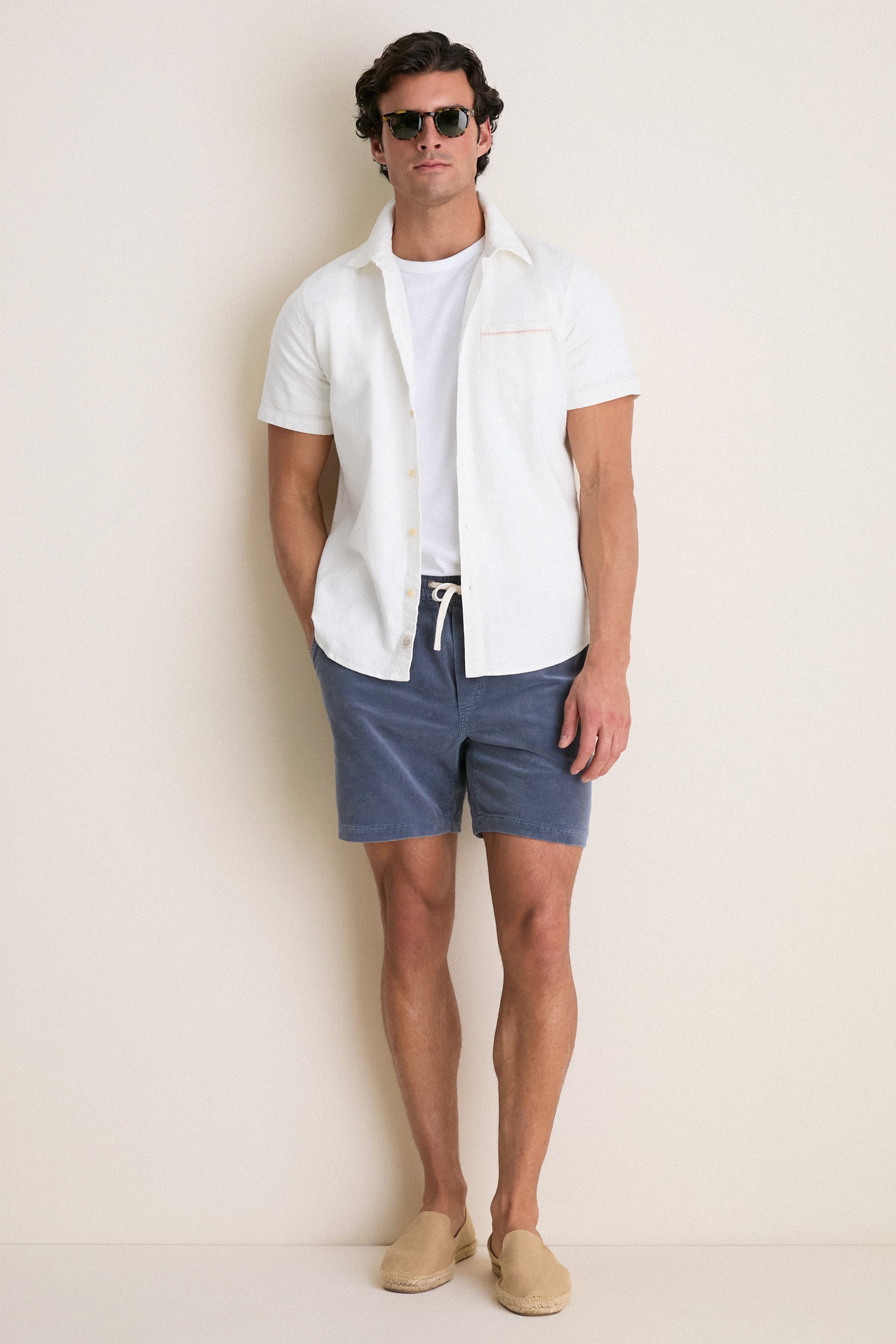 Man wearing a White Classic Stretch Selvage Shirt, embodying an effortless, high-end style with short sleeves and a front button placket, paired with navy drawstring shorts.