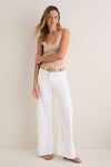 Model wearing the classic Pinch of Salt The Lemon Twist Skimp: a sleeveless beige knit top, high-waisted white pants, and tan sandals; accessorized with gold jewelry for an effortless, high-end look.