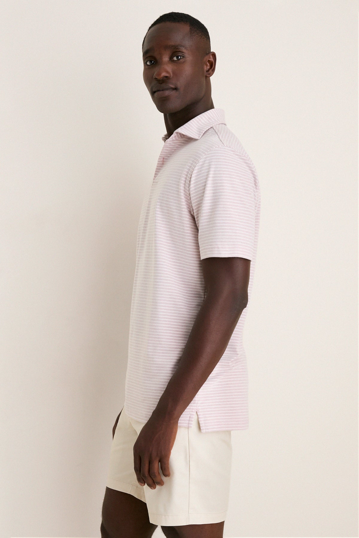 Person in profile wearing Peter Millar's Faded Scarlet Stripe Albatross Cotton Blend Pique Polo, exemplifying classic elegance with a high-end, effortless look featuring mother-of-pearl buttons.