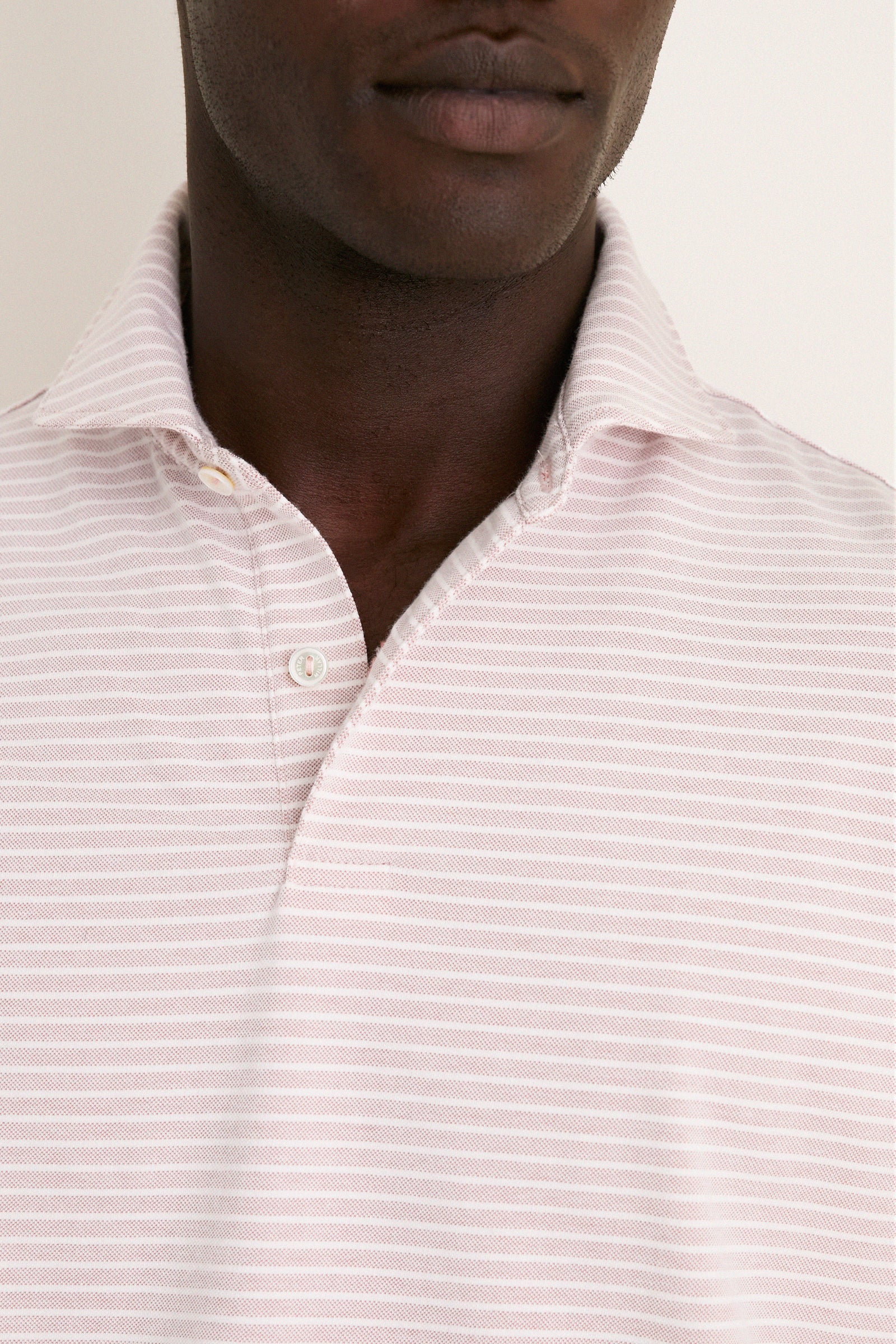Close-up of a person wearing Peter Millar's Faded Scarlet Stripe Albatross Cotton Blend Pique Polo, highlighting classic collar design and effortless, high-end craftsmanship.