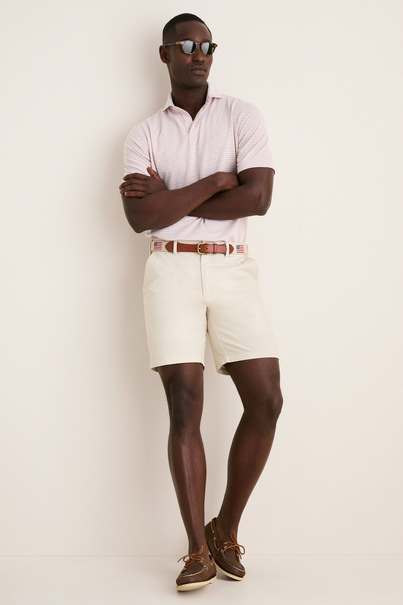 Man in Faded Scarlet Stripe Albatross Cotton Blend Pique Polo and cream shorts, embodying a classic, effortless style with high-end, fun details like tortoiseshell sunglasses and boat shoes.