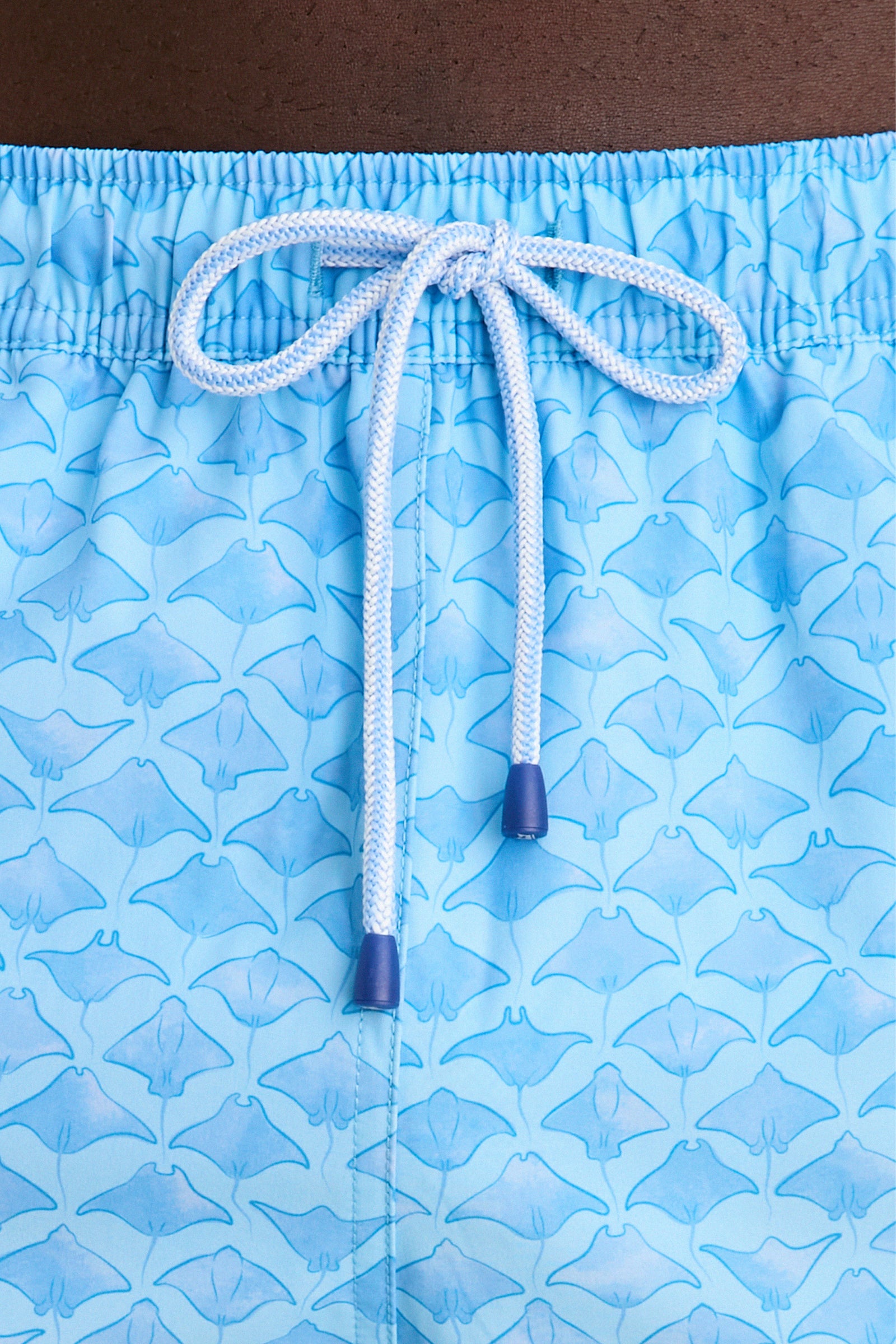 Close-up of Crystal Sea Coronado Swim Trunk showcasing light blue fabric with manta-ray pattern, elastic waist, and white drawstring, embodying Tuckernuck's effortless, high-end style.
