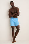Fit man models Crystal Sea Coronado Swim Trunk, showcasing classic, effortless style with light-blue geometric pattern, elastic waist, and quick-drying fabric. Perfect for fun, high-end beachwear.