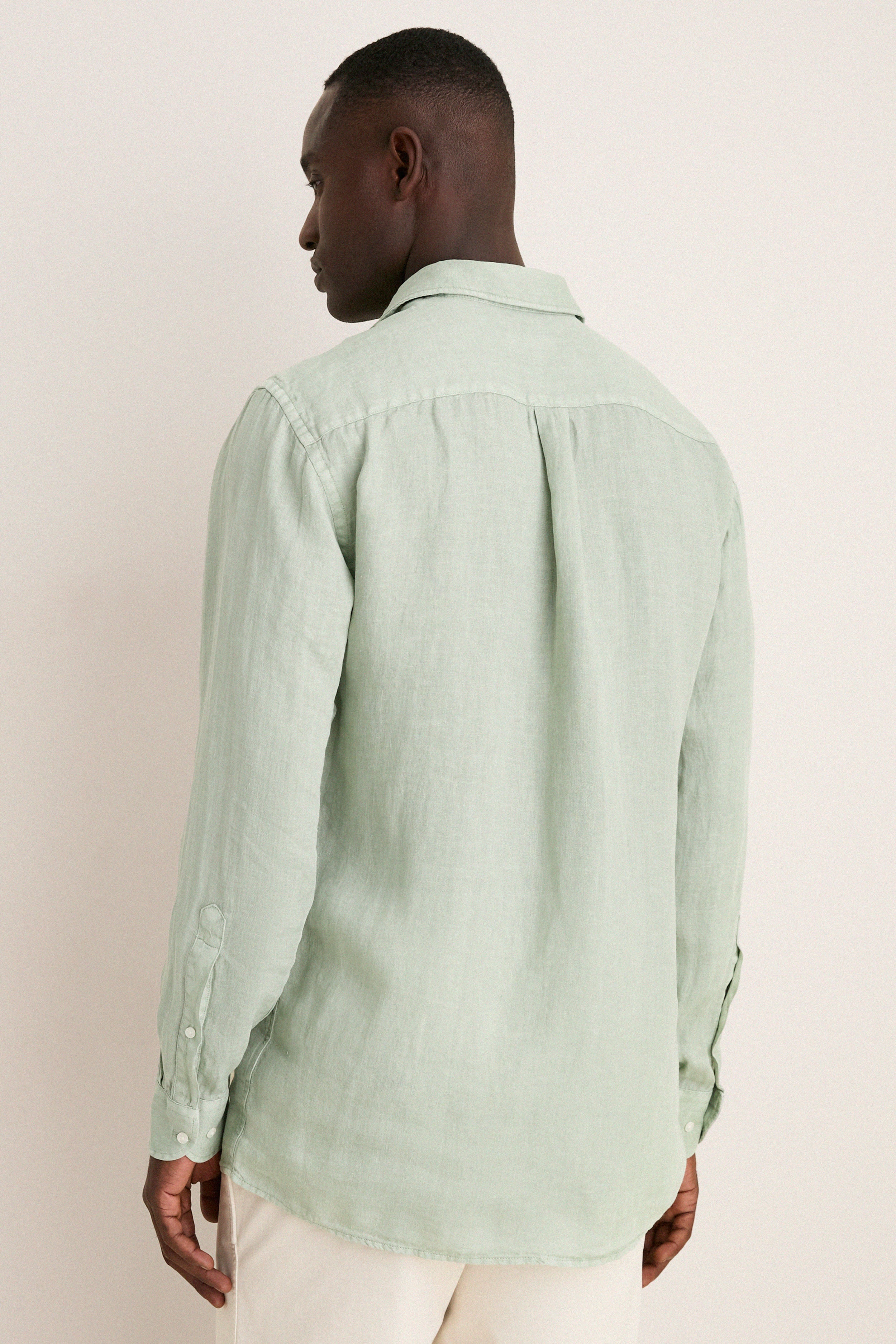 Back view of a man in a classic, light sage-green Grandview Shoreside Linen Sports Shirt, embodying effortless, high-end style with a modern twist.