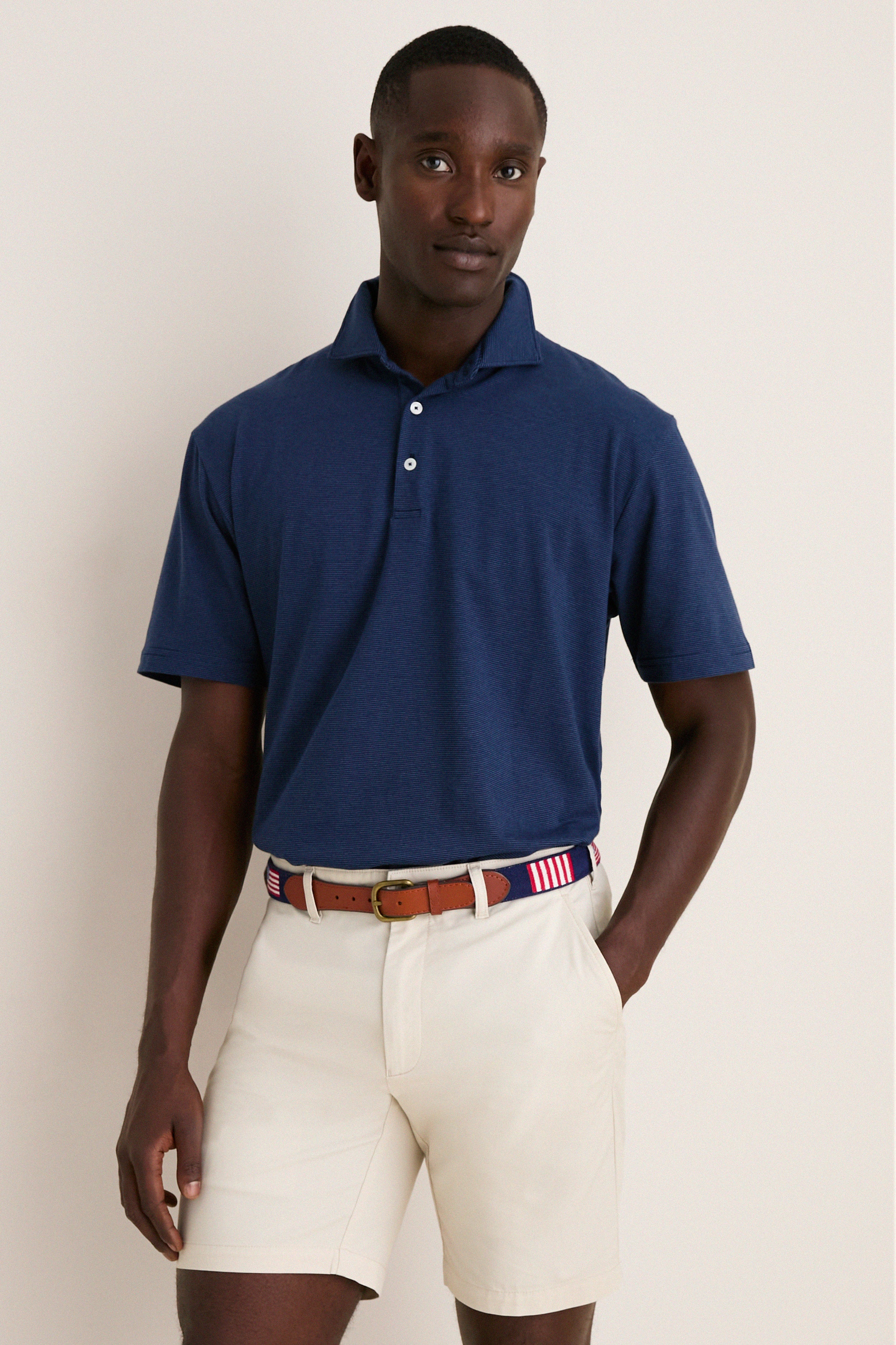 Young man models the Navy Ryles Crown Flex Cotton Polo, showcasing its classic cutaway collar and effortless, high-end style, paired with beige chino shorts and a striped belt.