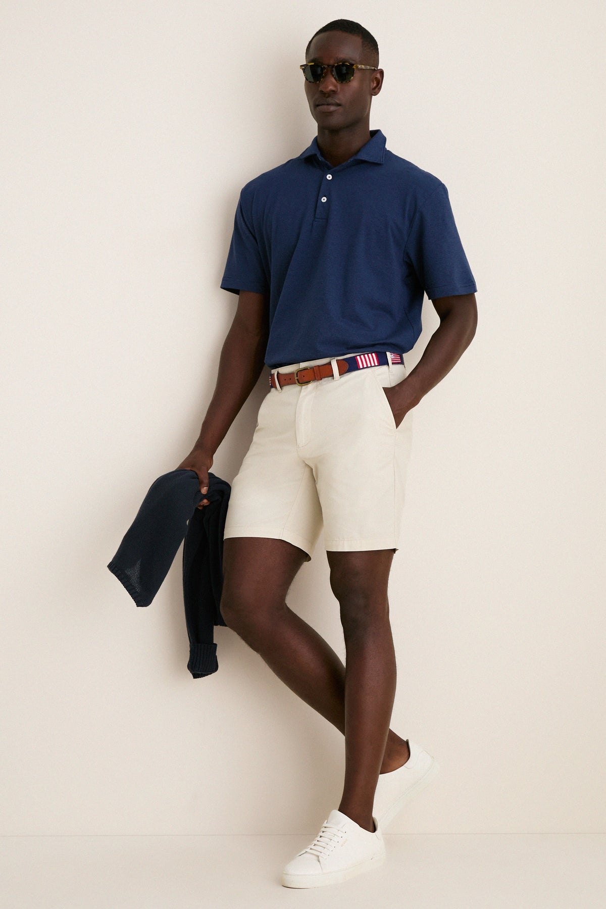 Model in navy Ryles Crown Flex Cotton Polo, classic cutaway collar, with beige chino shorts and red-white belt, embodying effortless, high-end style.