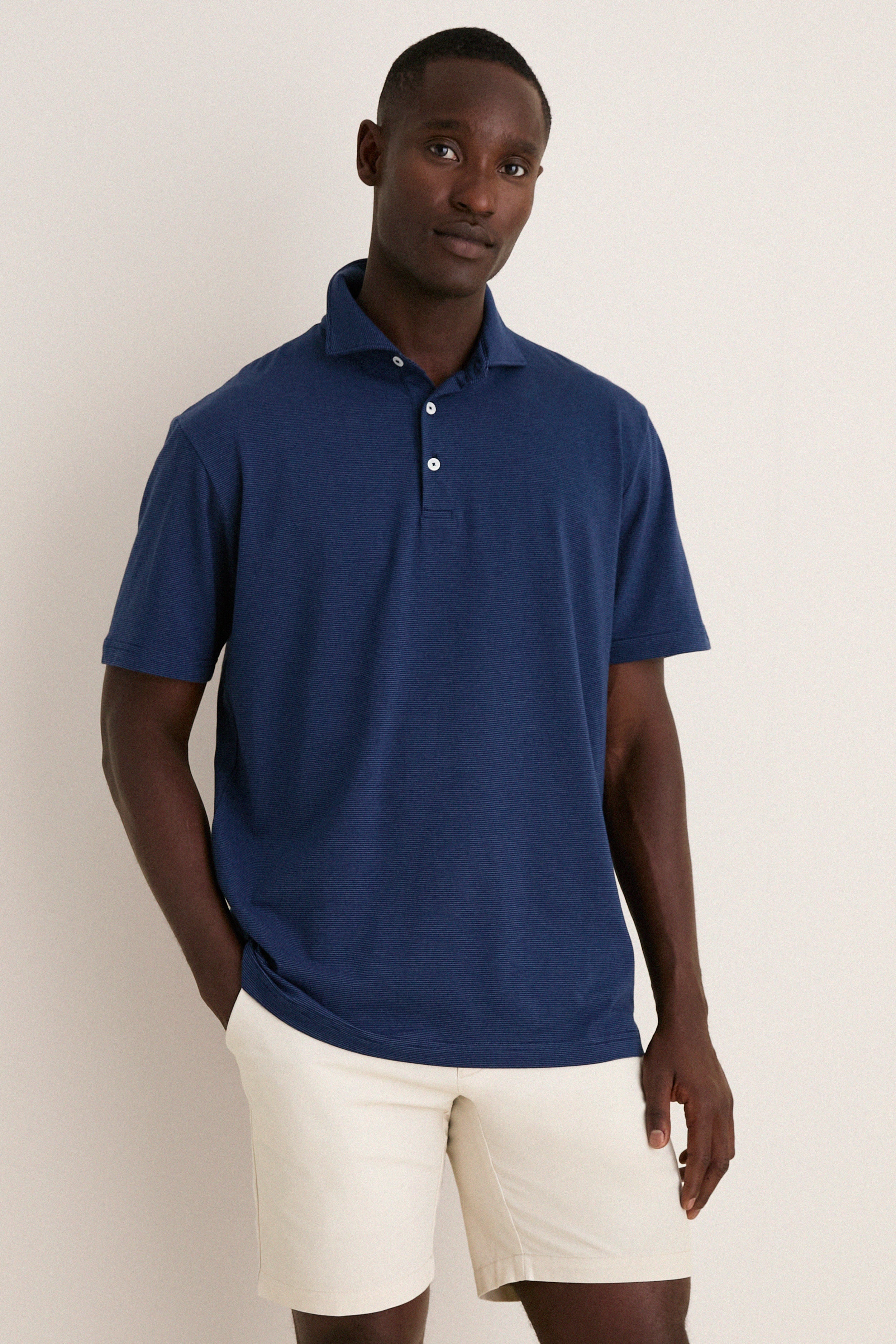 Man wearing the Navy Ryles Crown Flex Cotton Polo with classic cutaway collar and beige shorts, embodying effortless, high-end style perfect for fun, casual occasions.