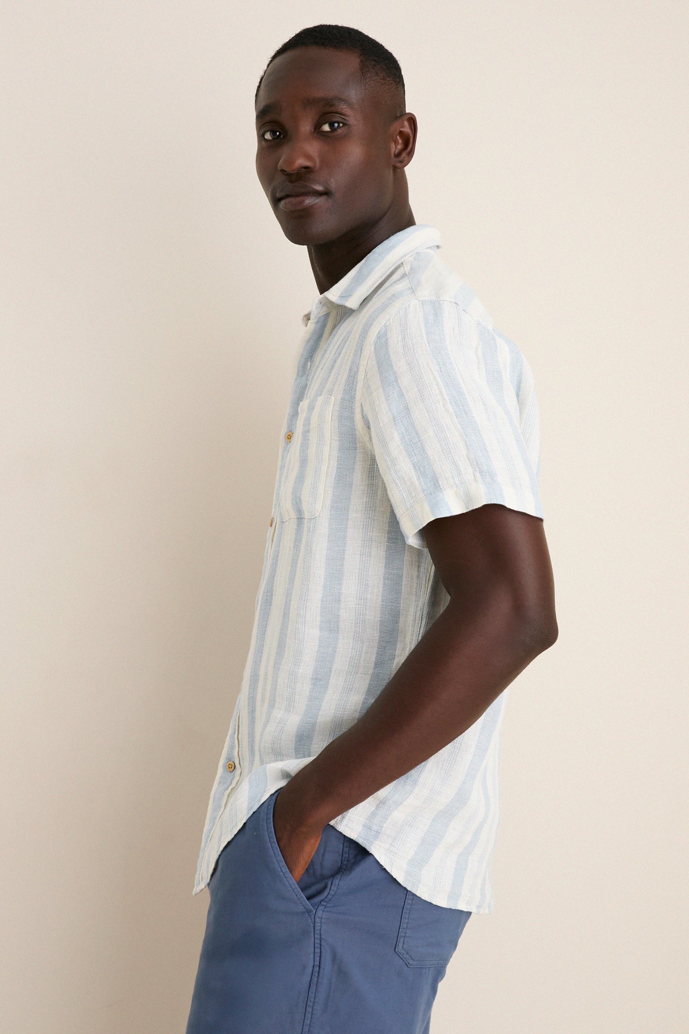 Person modeling the Island Blue Stripe Palma Linen Shirt, showcasing its classic, effortless style with a relaxed fit and front chest pocket, perfect for a fun, high-end summer look.