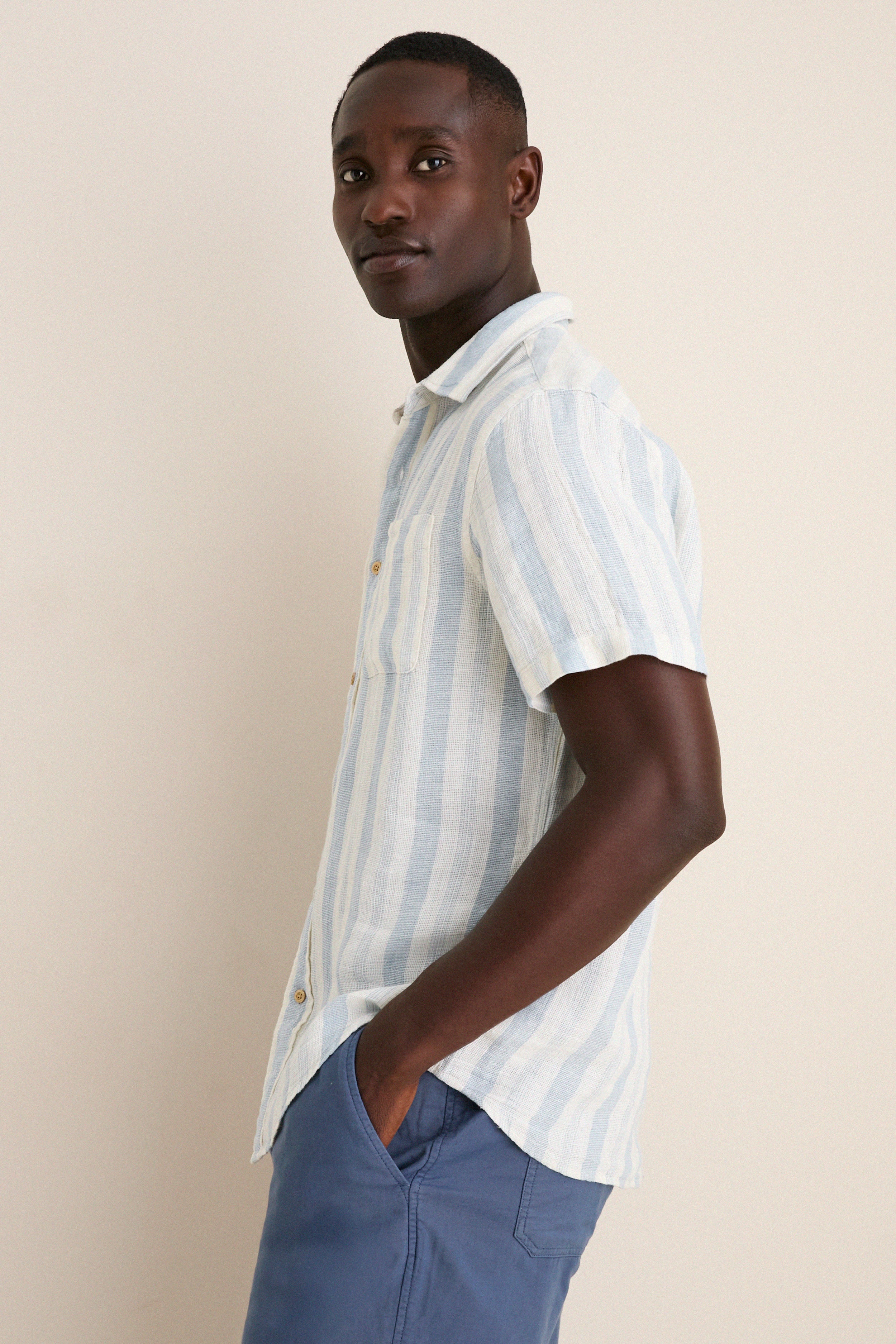 Person modeling the Island Blue Stripe Palma Linen Shirt, showcasing its classic, effortless style with a relaxed fit and front chest pocket, perfect for a fun, high-end summer look.
