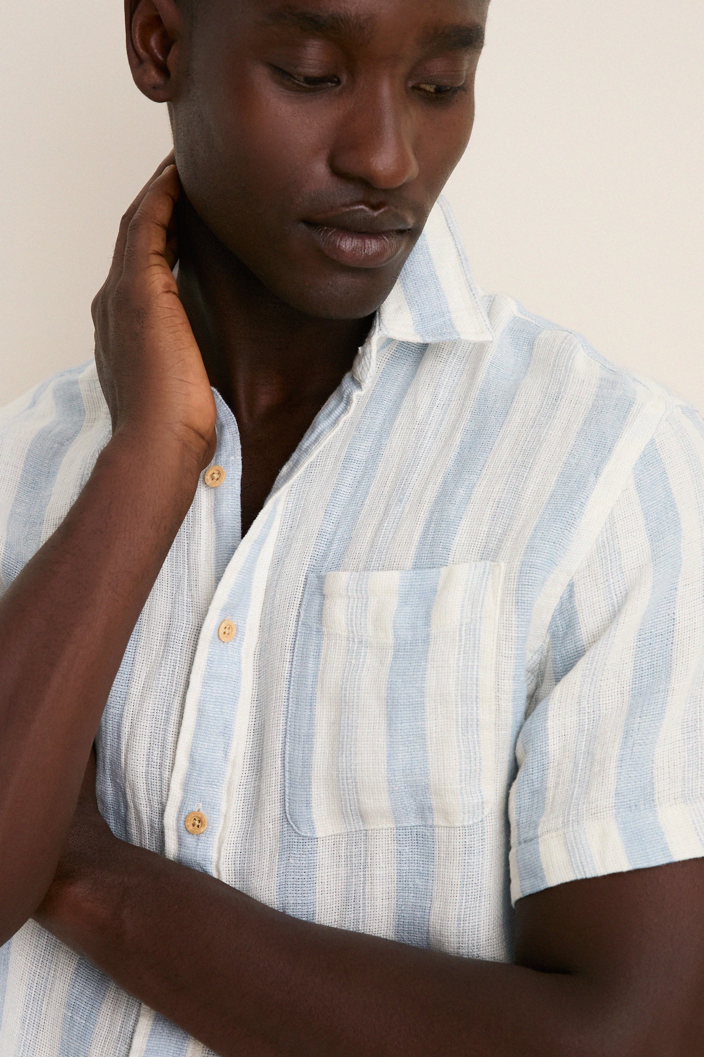 Person wearing the Island Blue Stripe Palma Linen Shirt with natural-wood buttons, showcasing a classic, effortless style. This high-end, fun piece features breathable linen and a chest pocket.