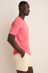Man wearing the Coral Red Sunwashed Pocket Tee, a classic, effortless, high-end T-shirt made from organic cotton, styled with light shorts for a fun, relaxed look.