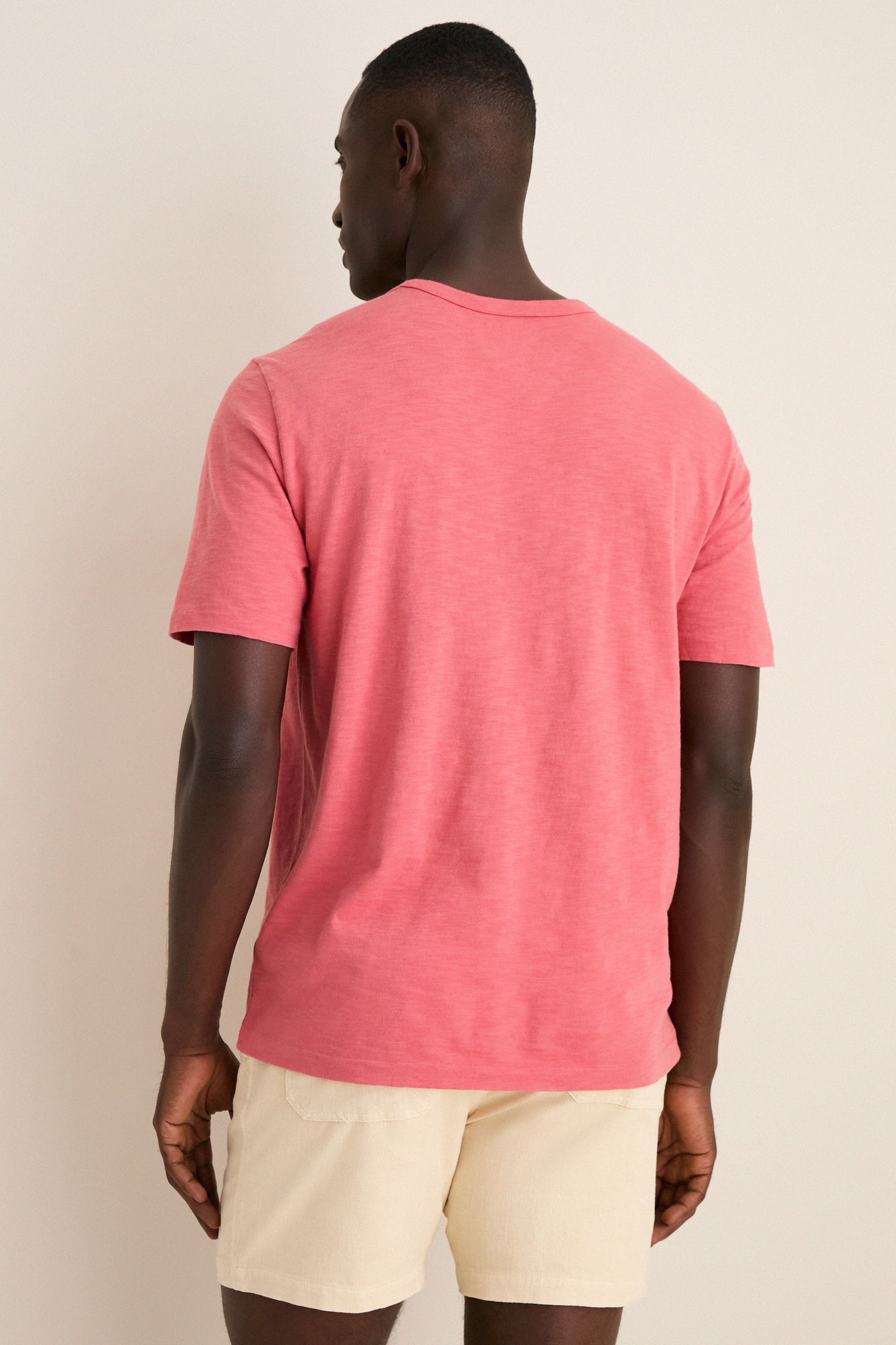 Man wearing a classic, effortless Coral Red Sunwashed Pocket Tee and light-beige shorts, showcasing a relaxed, high-end style perfect for fun, off-duty adventures.