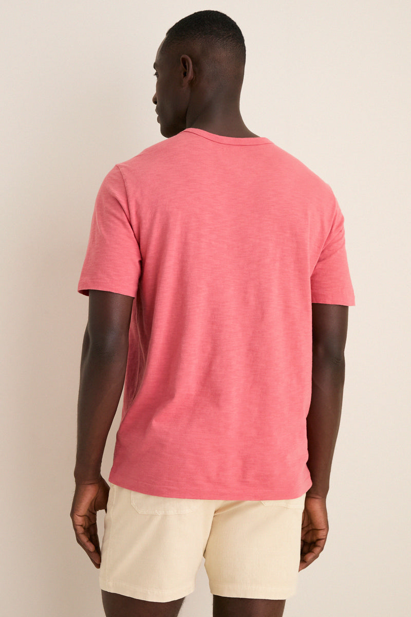 Man wearing a classic, effortless Coral Red Sunwashed Pocket Tee and light-beige shorts, showcasing a relaxed, high-end style perfect for fun, off-duty adventures.