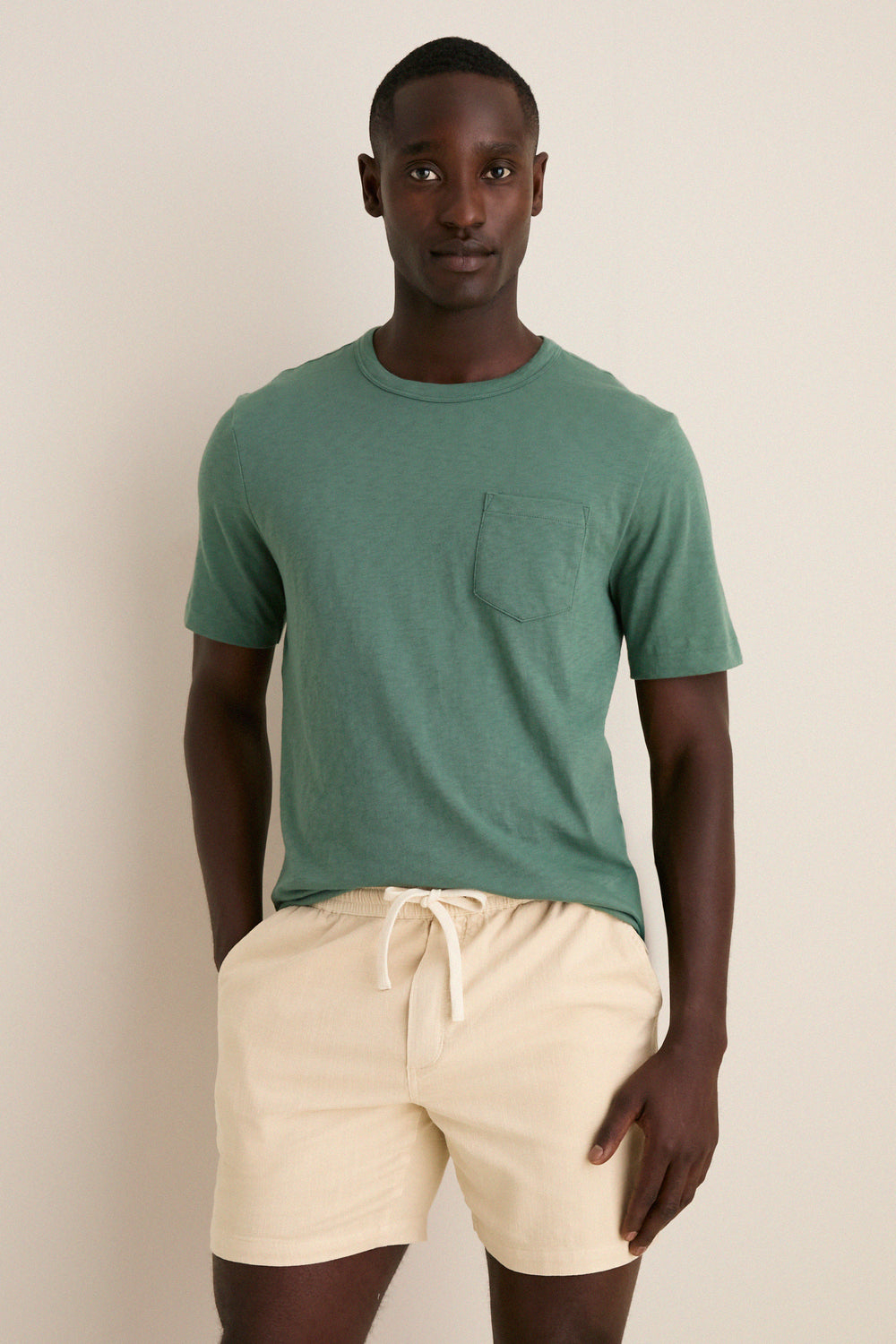 Young man in a classic Island Spruce Sunwashed Pocket Tee, effortlessly styled with beige drawstring shorts, embodying a high-end, fun, and relaxed vibe.