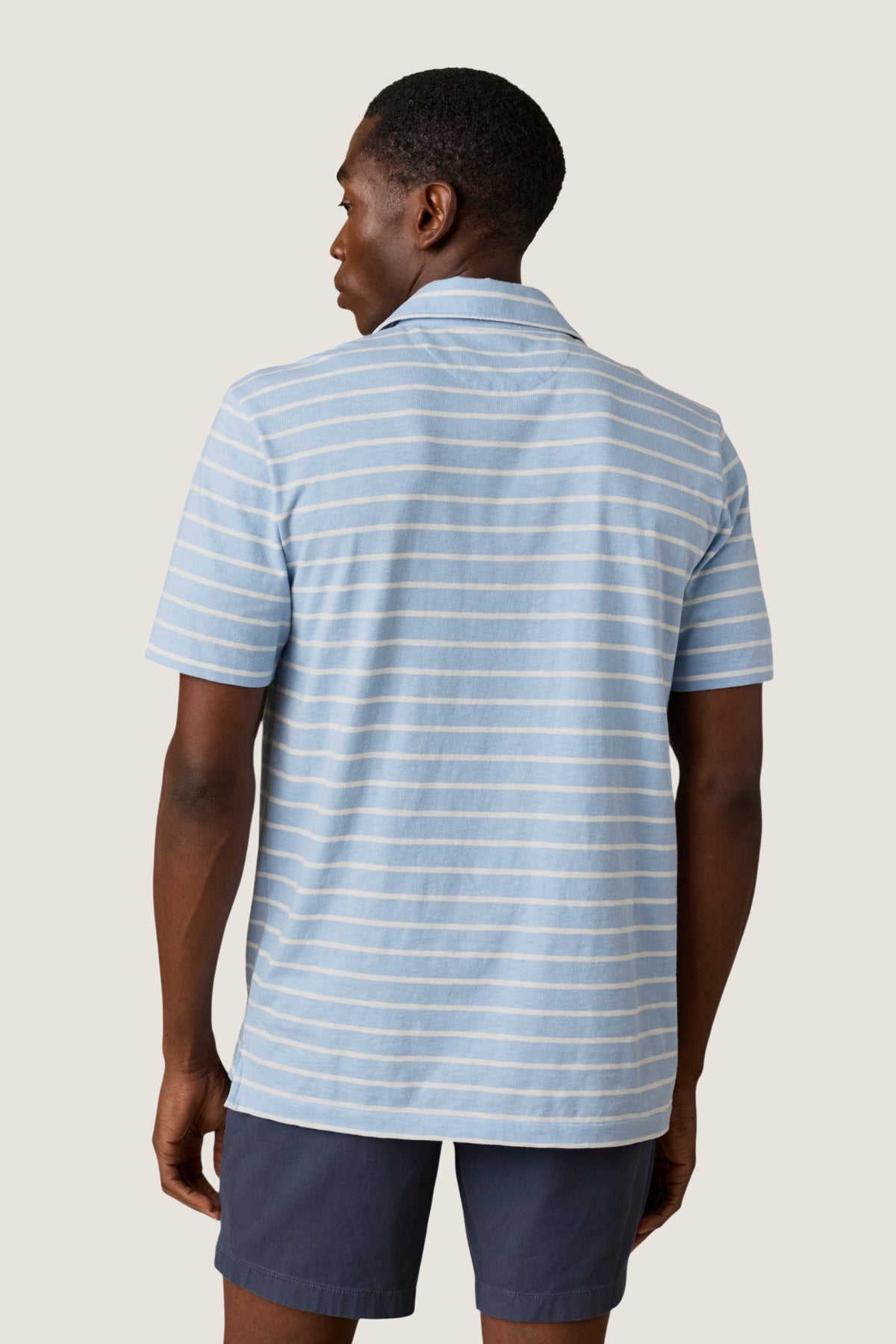 Person wearing the classic Bermuda Sail Stripe Sunwashed Tee Shirt Polo with thin stripes, exuding an effortless, high-end style against a neutral background, embodying Tuckernuck's fun shopping experience.