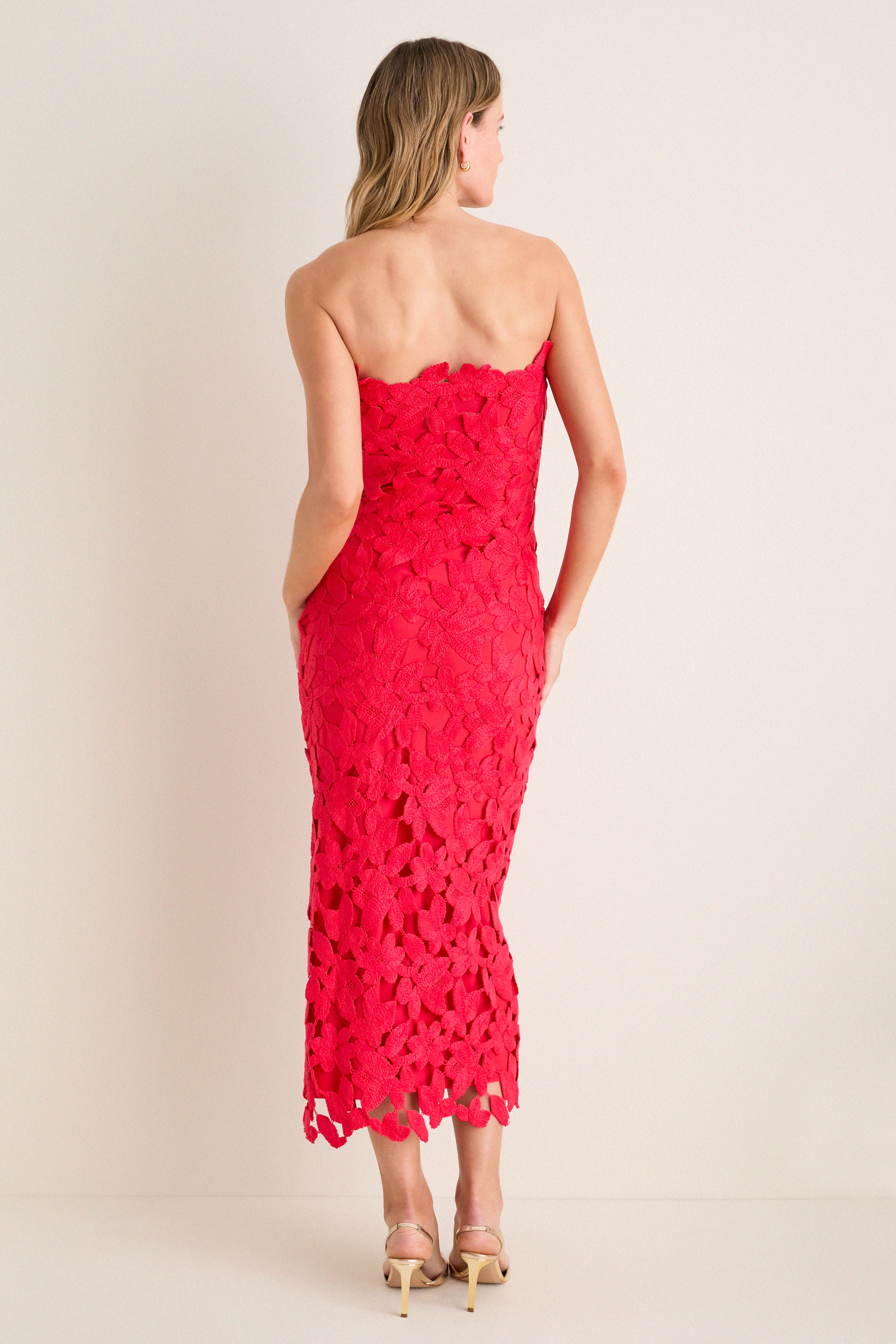 Woman in classic Cherry Red Philomena Midi Dress, strapless with floral crochet and scalloped hem, paired with nude high-heeled sandals, exuding effortless, high-end style.