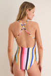 Woman wearing Pariti Fiesta Retiro One Piece swimsuit with multicolored stripes, featuring X-shaped straps, exuding classic, effortless style with a touch of high-end, fun elegance.