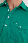Close-up of a classic, high-end green polo shirt, featuring a 4-button placket, chest pocket with embroidery, and subtle ribbed texture, embodying effortless style and fun.
