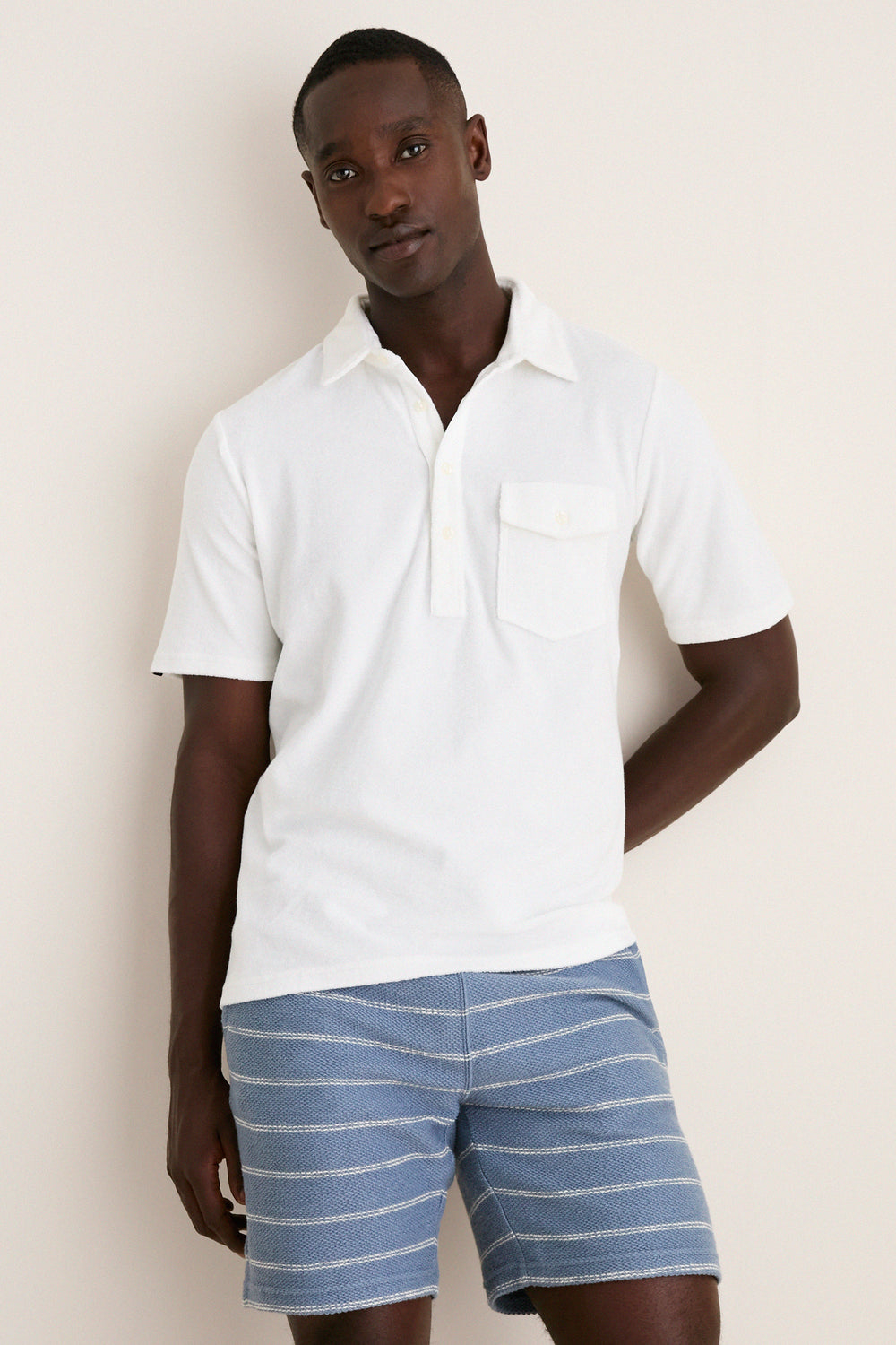 Dark-skinned man wearing a classic, high-end White Lotus Terrycloth Players Shirt, effortlessly styled with light blue knit shorts, exuding a fun, relaxed vibe.
