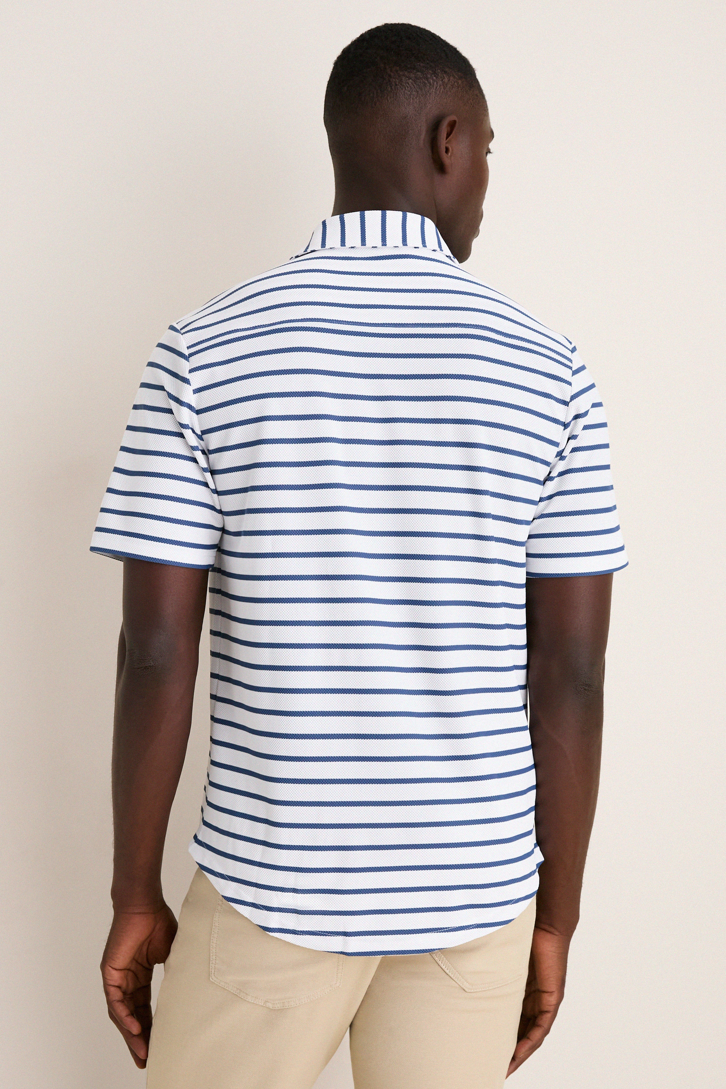 Model in a classic White Performance Pique Knit Button Down, featuring effortless navy-blue stripes and light-beige pants, embodying a high-end, fun style.