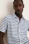 Young man wearing the White Performance Pique Knit Button Down, showcasing its classic, effortless style with navy stripes, flap pocket, and spread collar. Perfect for high-end, fun adventures.