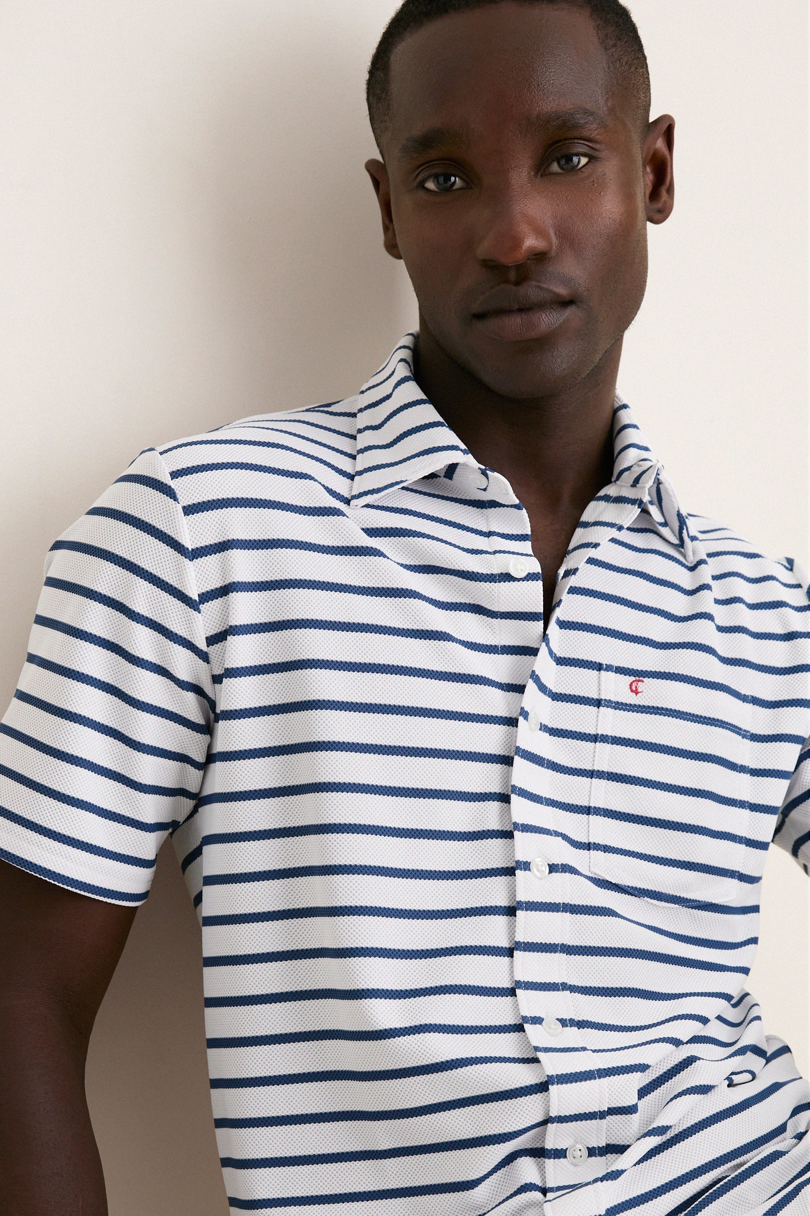 Young man wearing the White Performance Pique Knit Button Down, showcasing its classic, effortless style with navy stripes, flap pocket, and spread collar. Perfect for high-end, fun adventures.