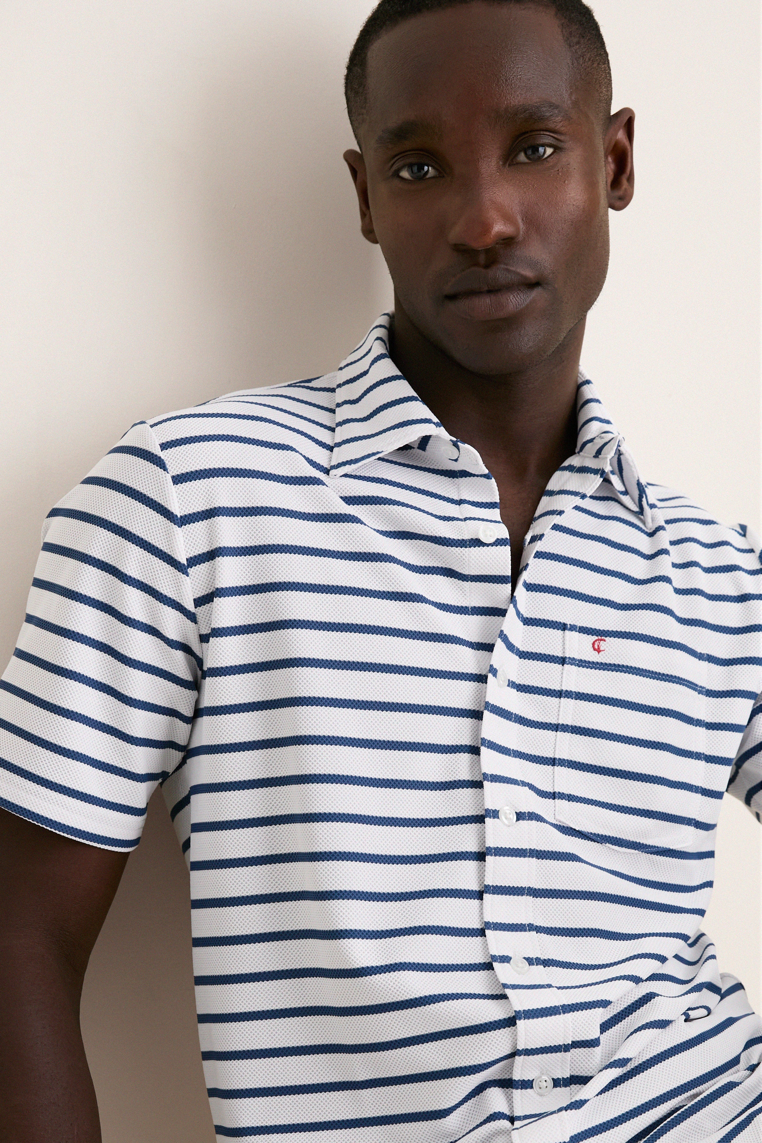 Young man wearing the White Performance Pique Knit Button Down, showcasing its classic, effortless style with navy stripes, flap pocket, and spread collar. Perfect for high-end, fun adventures.