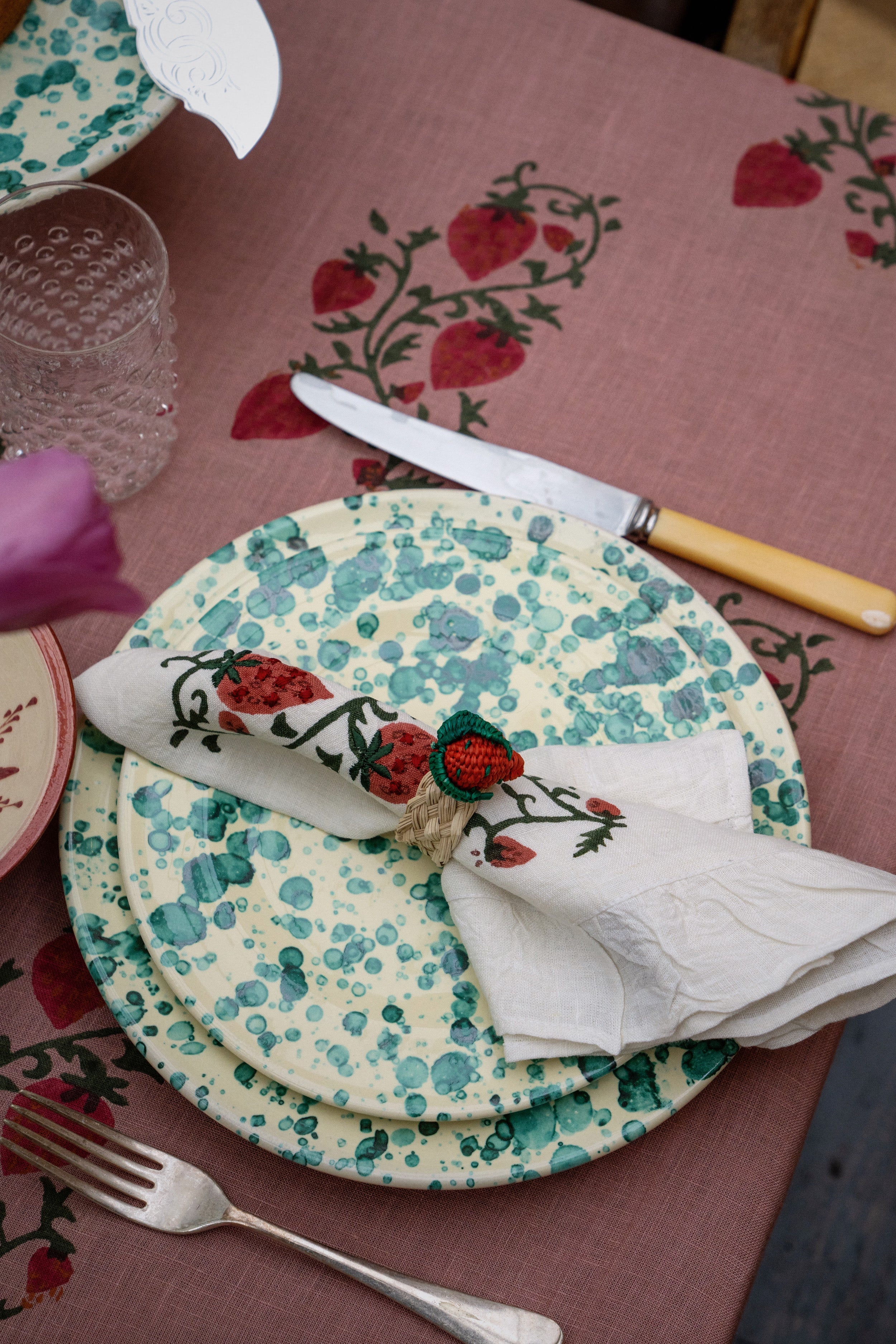 Classic and effortless, the Yellow and Verde Splatter Dinner Plate showcases a fun teal-green bubble glaze, perfect for high-end entertaining with a vibrant strawberry-themed setting.