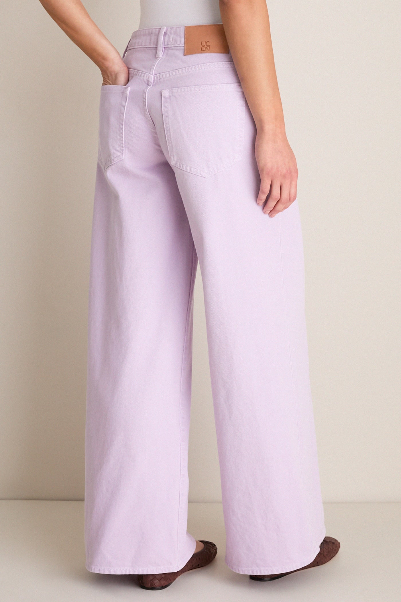 Model wearing Wisteria Zephyr Mid Rise Wide Leg Jean, showcasing classic, effortless style with wide legs, low waist, and patch pockets, paired with woven-leather flats.