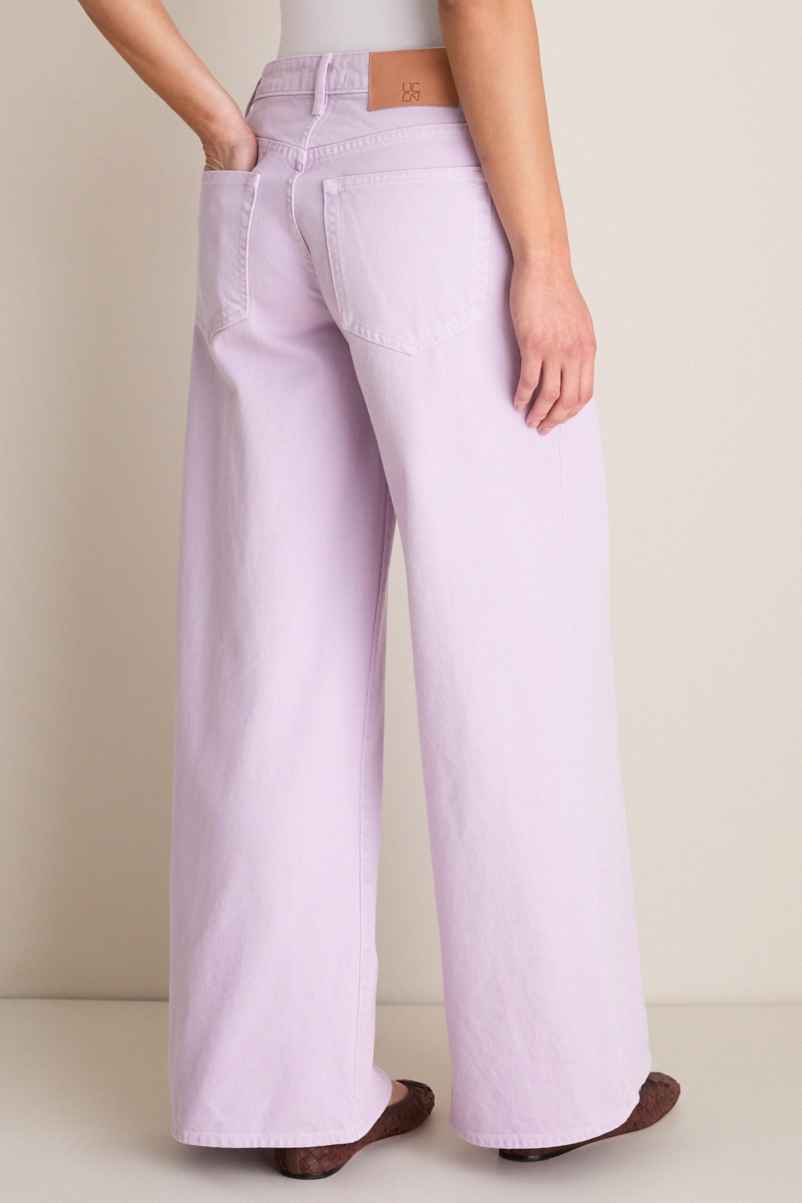 Model wearing Wisteria Zephyr Mid Rise Wide Leg Jean, showcasing classic, effortless style with wide legs, low waist, and patch pockets, paired with woven-leather flats.
