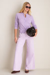 Model showcases Wisteria Zephyr Mid Rise Wide Leg Jean, exuding classic, effortless style with a fun, high-end look, paired with woven flats and basket handbag.