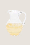 Amalia Glass Round Pitcher, a classic, high-end, mouth-blown glass jug with a swirling thread and berry design, half-filled with a light-colored drink over ice, embodying effortless elegance.
