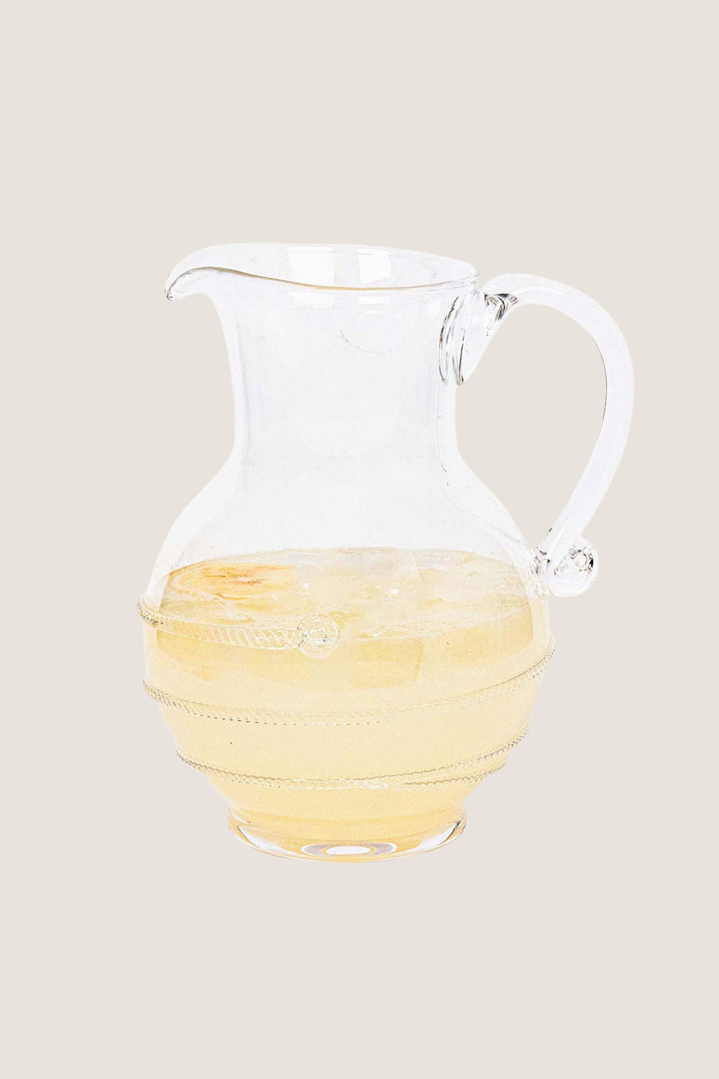 Amalia Glass Round Pitcher, a classic, high-end, mouth-blown glass jug with a swirling thread and berry design, half-filled with a light-colored drink over ice, embodying effortless elegance.