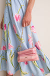 Person holding Rose Water Malaya Clutch, an asymmetrical, marbled acrylic bag with gold-link chain, paired with a classic floral dress for an effortless, high-end look.