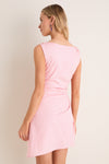 Woman in light-pink Tulip Callie Mini Dress with asymmetrical hem, showcasing classic elegance. Features ruched waist and twisted sleeves for an effortless, high-end look.