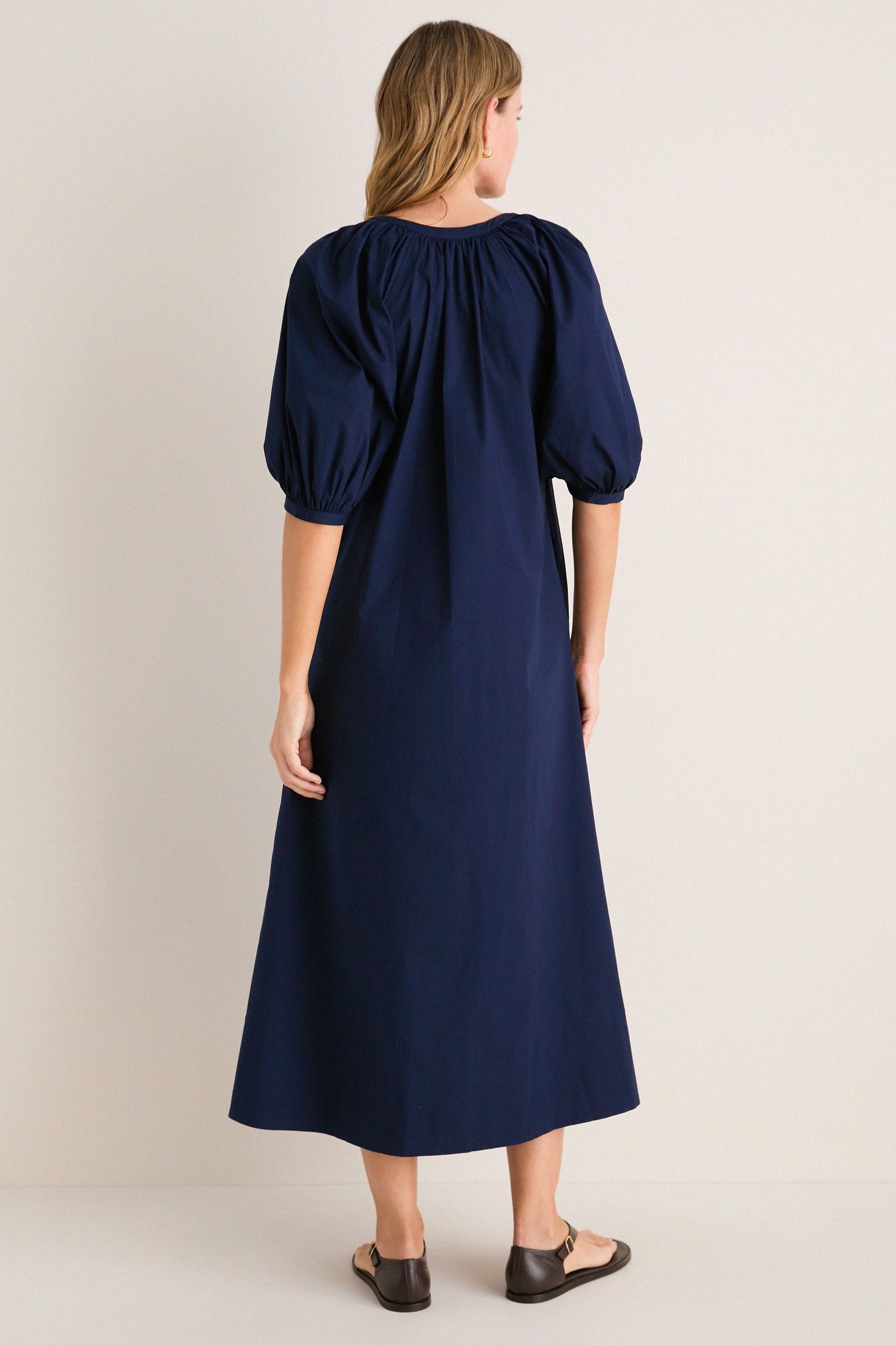Back view of a woman in the classic Navy Vincent Dress with puff sleeves and button-down front, styled with simple sandals for an effortless, high-end look.