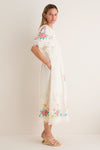 Woman models the Multi Astrid Embroidery Short Sleeve Midi Dress, showcasing its classic cape-style yoke, effortless floral motifs, and fun eyelet lace details, paired with high-end wedge sandals.