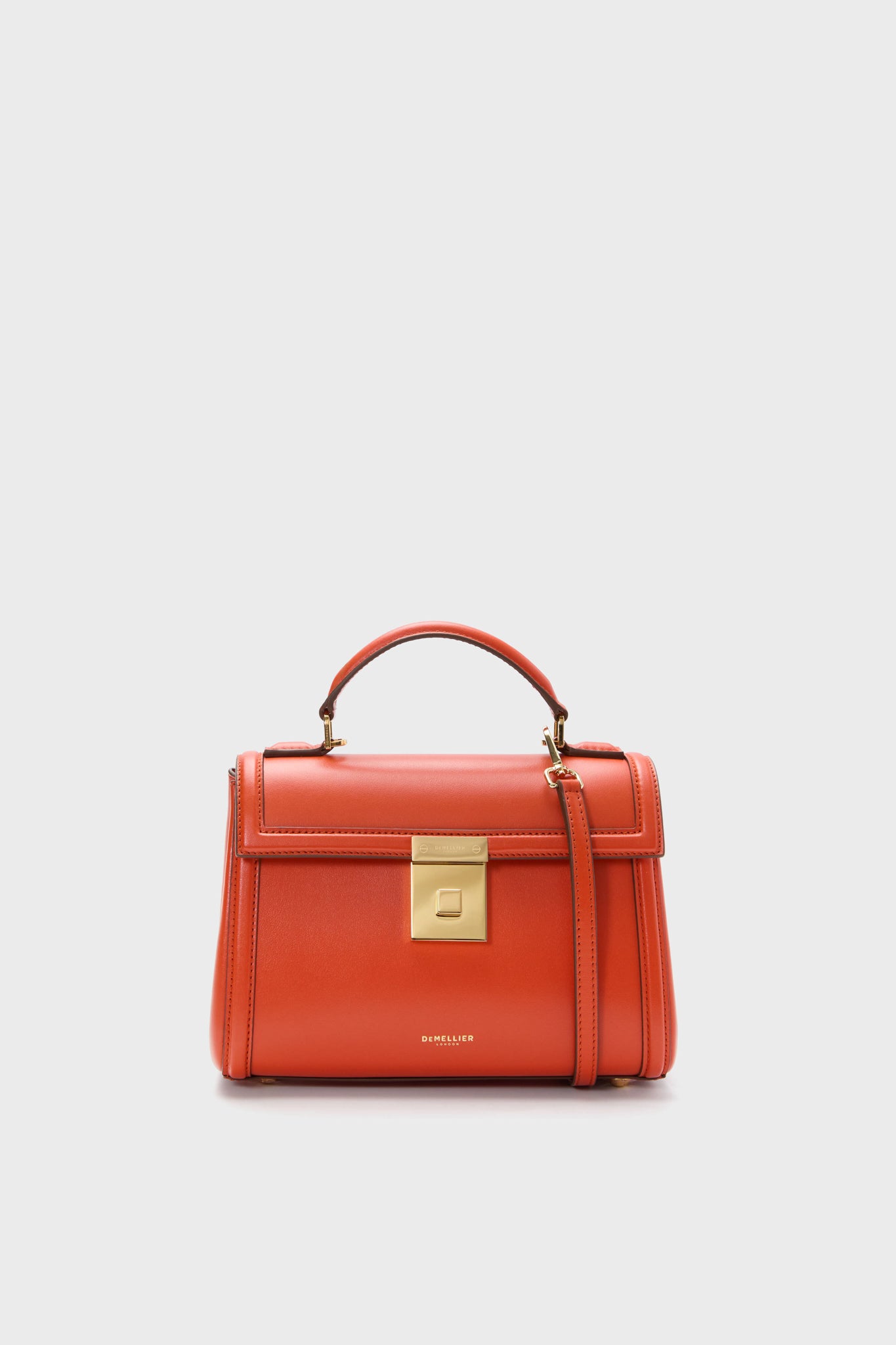 The Demellier structured burnt orange top handle bag, handmade from sustainable Italian leather, features a gold-tone rectangular clasp and adjustable shoulder strap. This elegant purse exudes timeless sophistication.