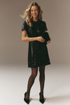 Young woman in a classic, high-end Black Sequin Roya Swing Mini Dress, exuding effortless fun, ideal for parties, paired with polka dot tights and pointed heels.