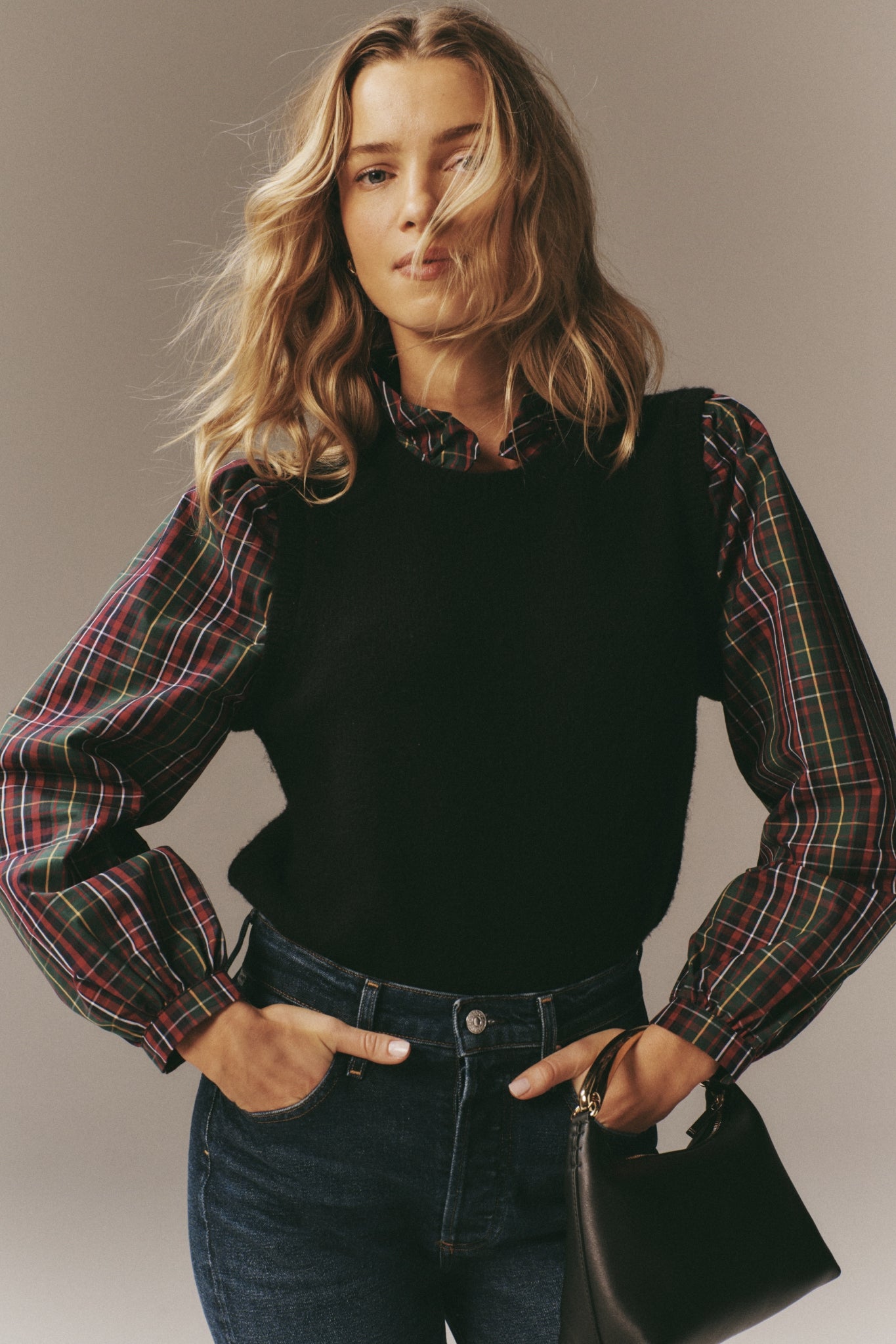 Young woman models the Tartan Ella Sweater Blouse, featuring a classic layered knit vest and plaid shirt, styled effortlessly with high-waisted jeans and chic handbag.