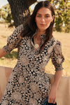Woman in a black and tan colored floral patterned dress with a large pendant necklace. 