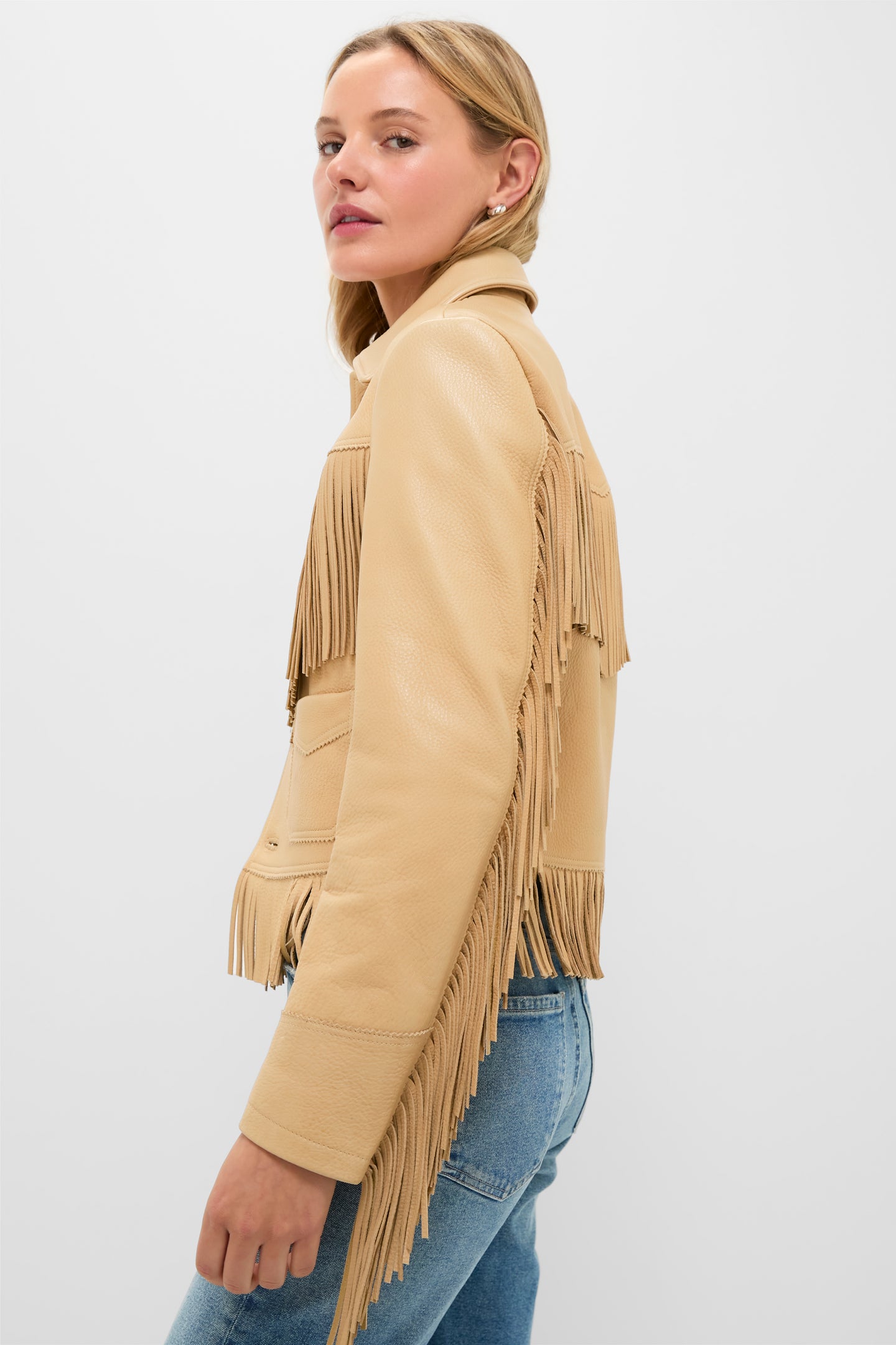 Young woman models a classic Tan Deerskin Fringe Jacket, showcasing its high-end, effortless Western flair with fringe detailing, perfect paired with denim for a fun, confident look.