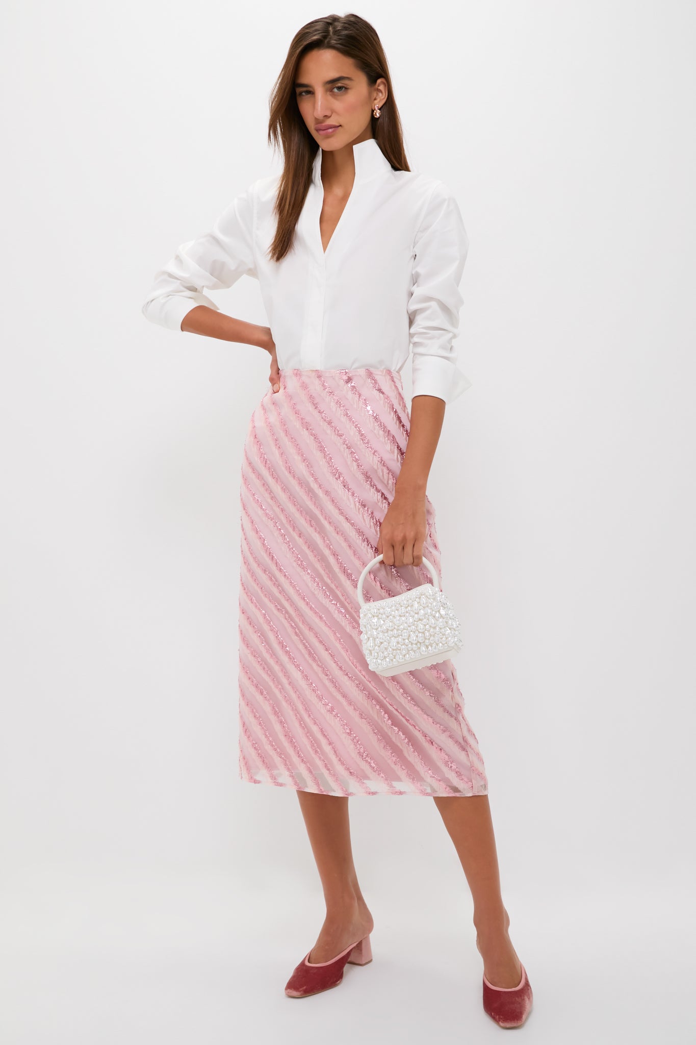 Woman wearing classic Soft Pink Shimmer Stripes Milan Midi Skirt, styled effortlessly with a crisp blouse and velvet mules; holding a beaded handbag for a fun, high-end look.