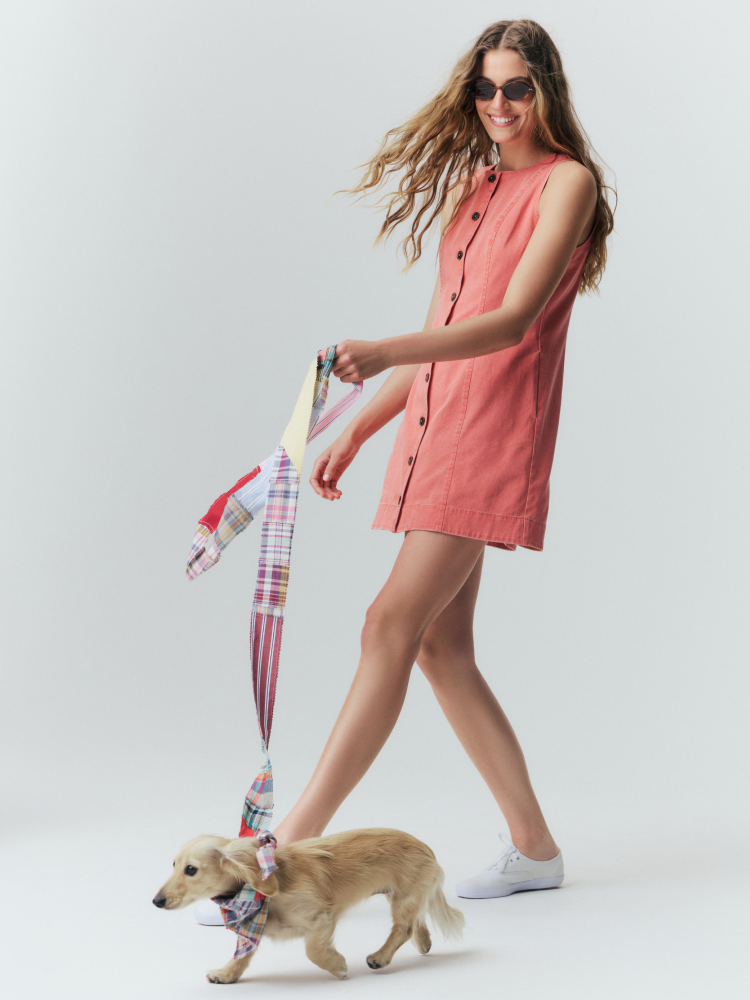 Woman wearing a red shift dress with buttons down the front walking a dog with a madras leash. 