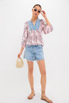 A woman models Bell by Alicia Bell: sunglasses, a boho blouse with printed yoke and blue embroidery, distressed denim shorts, strappy sandals, and a small woven handbag.
